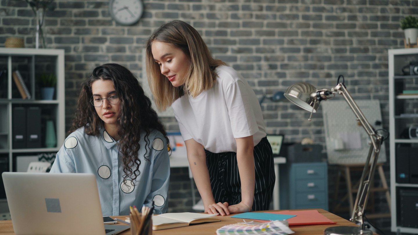 Due donne collaborano su un laptop a una scrivania moderna in ufficio.